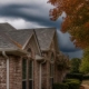 North Texas brick home with fall leaves at the gutter and a cold front rolling in behind the roof